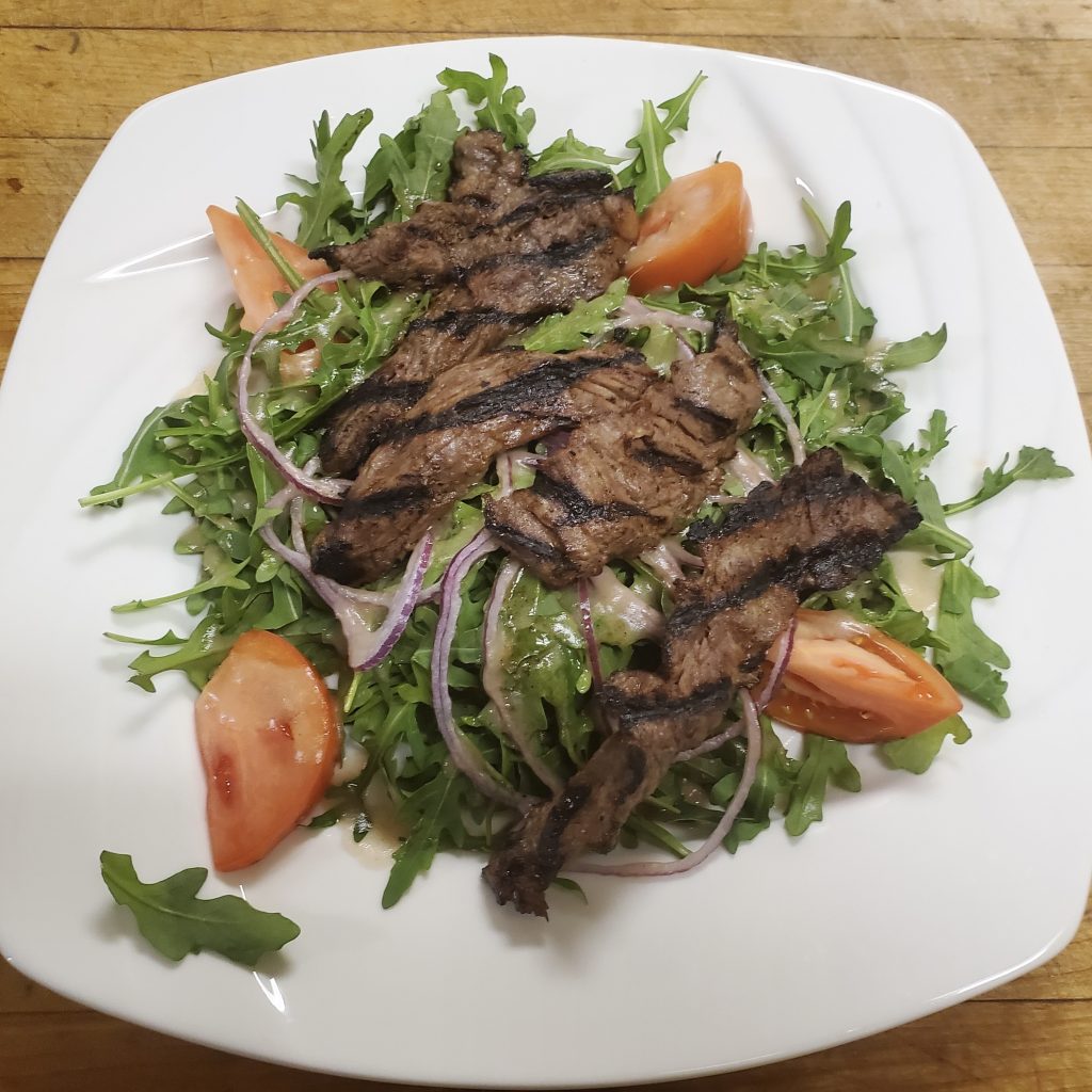 marinated steak strips, red onion, tomato wedges, and blue cheese crumbles over a bed of arugula with honey ginger dressing